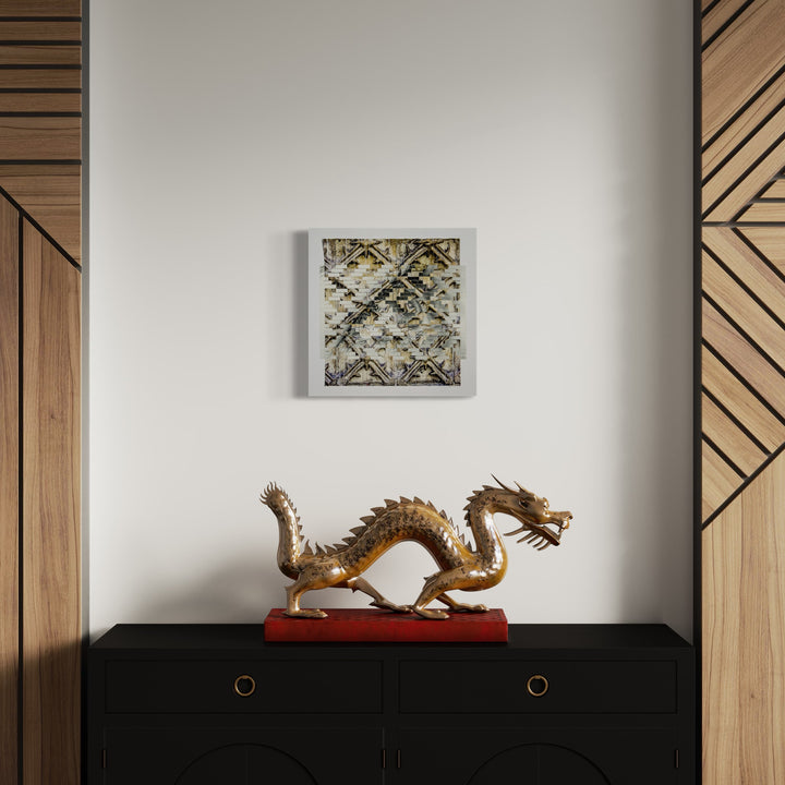 The artwork 'Indirection' by Kiana Honarmand features intricately hand-cut and woven giclee prints arranged in a geometric pattern, showcasing metallic gold and silver tones in an 18x18 inch square format. The piece displays layered textures creating a dimensional abstract design with intersecting lines and diamond motifs. Mounted above a decorative golden dragon sculpture.