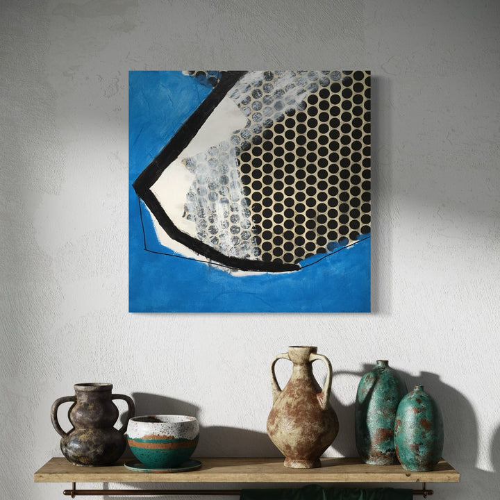 A photo of the artwork Black Dots with Blue, by Diane Englander, hanging on a wall.