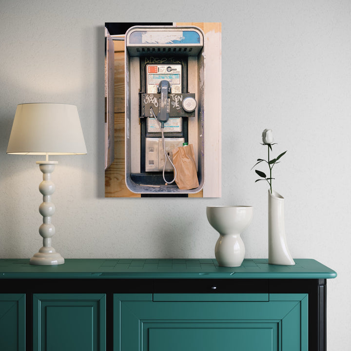 The artwork 'Brown Bag' features a vintage payphone installation with a brown paper bag hanging from the receiver, captured in an editioned photograph. The composition shows metallic details, a blue-framed phone booth enclosure, and industrial elements against a textured wall. 30x20 inches photographic print by Dirk Westphal.