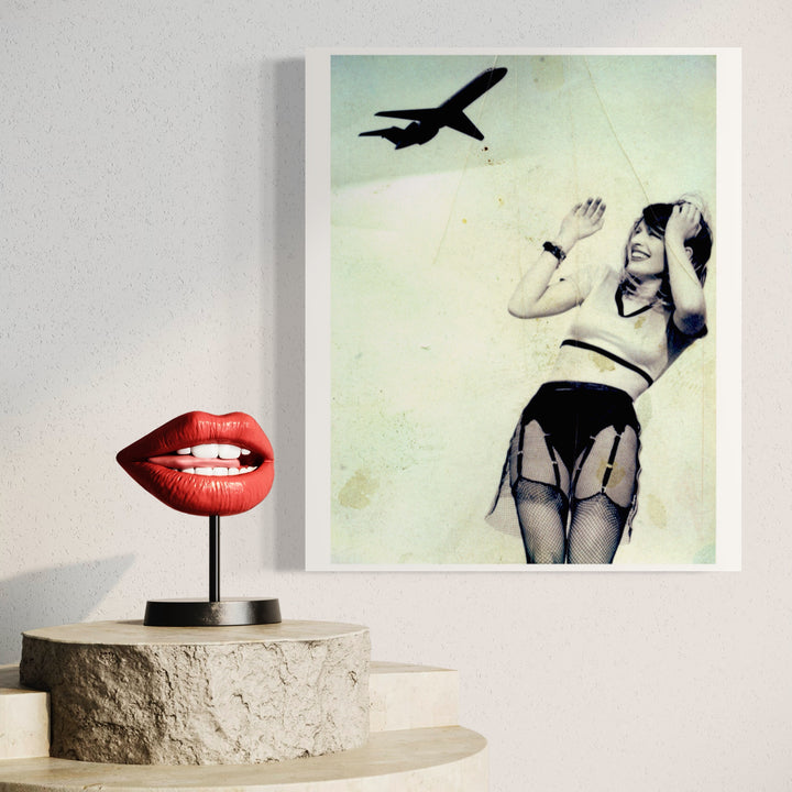 The artwork 'Cherry with Plane on the Roof' by Dirk Westphal features a striking red lip sculpture mounted on a concrete pedestal alongside a vintage-style photograph with a mint green background showing a silhouette of a plane. The photograph presents a dramatic composition in black and white tones. A signed editioned photo, 24x20 inches, by Dirk Westphal.