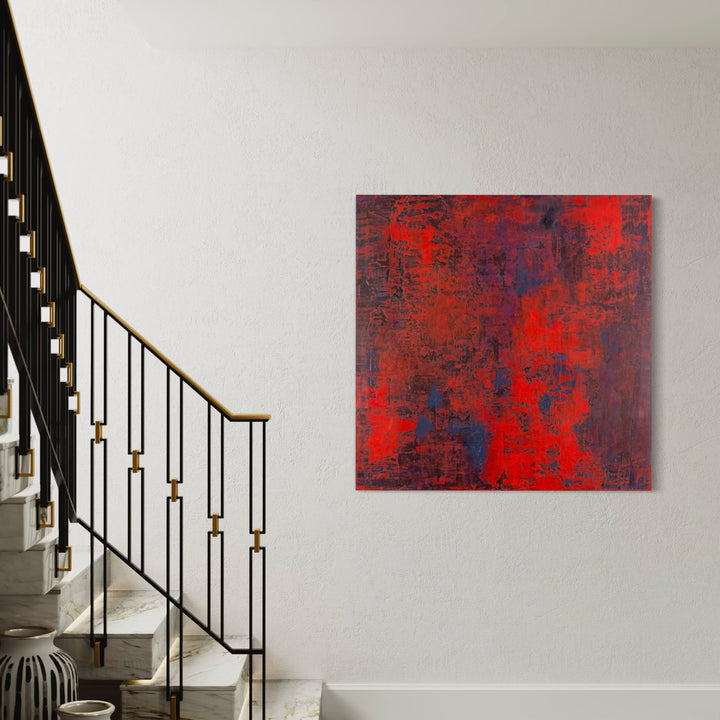 The artwork 'Crimson Aura' by Nicole Hitchcock features vibrant layers of deep crimson and scarlet acrylic paint intermingled with rich navy undertones, creating a textured abstract composition. The 48x48 inch canvas showcases a distressed, weathered effect with bold brushstrokes and subtle color variations, giving depth and movement to the modern wall art piece.