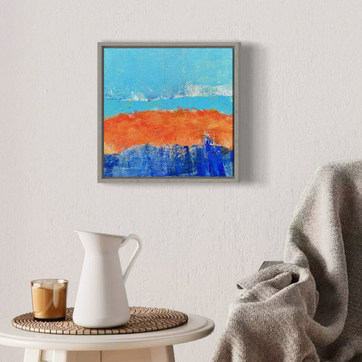 The artwork 'Dancing on the Shore' by Karen L. Burns features vibrant abstract landscape with three distinct horizontal bands: a bright turquoise sky, a bold orange-red shoreline, and deep cobalt blue waters. The acrylic painting's textured surface creates dynamic movement, with subtle white splashes where colors meet, displayed in a modern gray frame. 12x12 inches abstract art by Karen L. Burns.