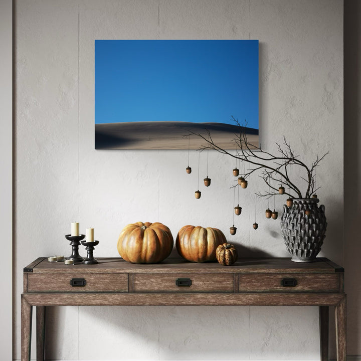 The artwork 'Dune' by Cavier Coleman features a minimalist desert landscape photograph showcasing smooth sandy dunes against a vivid blue sky. The image captures the stark contrast between golden sand ripples and the azure horizon, creating a serene and meditative composition. The dramatic curves of the dunes emphasize natural patterns and textures in this 24x36 inch photographic print by Cavier Coleman.