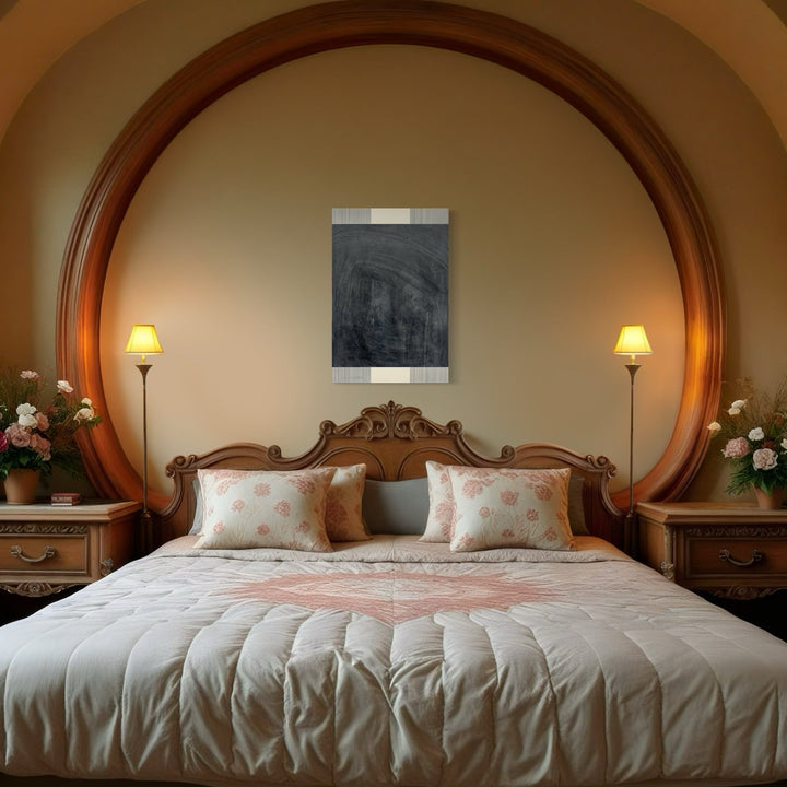 The artwork 'Erasure 44' by Erika Mahr displayed in an elegant bedroom setting with ornate wooden headboard, features abstract charcoal and paint marks on panel. Dark, moody composition in grayscale tones, mounted between two wall sconces, creates striking contrast against warm beige wall within circular archway.