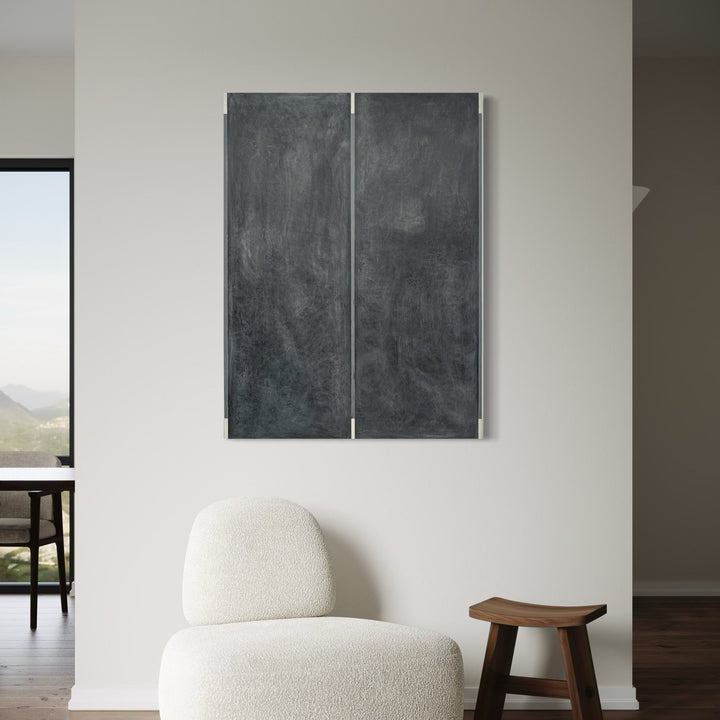 The artwork 'Erasure 47' by Erika Mahr features a diptych composition in deep charcoal tones, with two vertical panels displaying textural, smoky surfaces. The minimalist abstract piece shows subtle gradients and gestural marks in graphite and paint, creating a contemplative atmosphere against a stark white wall.