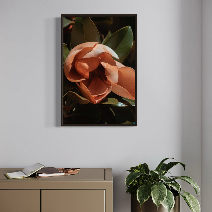 The artwork 'Flower Study II' by Eunice Pais features a close-up photographic capture of a delicate salmon-pink magnolia bloom against a dark background. The composition highlights the flower's layered petals casting soft shadows, surrounded by deep green glossy leaves, creating a dramatic botanical portrait with rich contrast and artistic lighting.