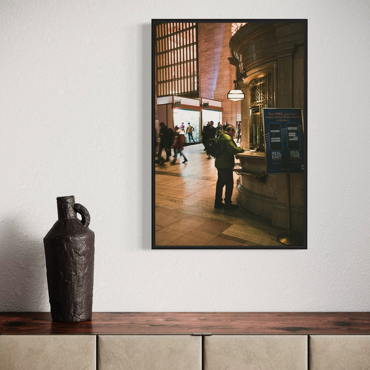 The artwork 'Get Me Home' by Dennis Maida captures a moody interior of Grand Central Terminal, featuring warm-lit architecture with soaring arched ceilings and classic stone columns. Silhouettes of commuters move through the bustling space, while dramatic natural light streams through the iconic tall windows, creating a cinematic urban atmosphere with rich amber and golden tones. By Dennis Maida.