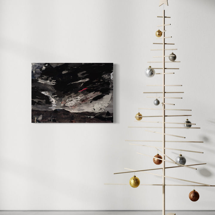 The artwork 'Hraun' by Marianne Barcellona features a dramatic mixed-media landscape with dark, turbulent clouds over a mountainous horizon. Bold black and gray brushstrokes create a moody atmosphere, with subtle red accents and textural elements achieved through ink, acrylic, and paper collage techniques, displayed beside a minimalist wooden Christmas tree decoration.