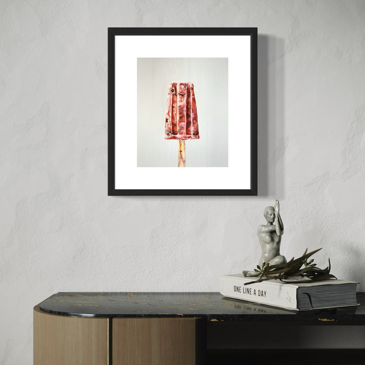 The artwork 'ICE BREAKER I' by Shweta Matai depicts a vibrant popsicle in rich red and white marbled tones, rendered in oil paint. The frozen treat shows intricate textural details and melting drips, set against a minimalist light background. The piece is elegantly displayed in a black frame with white matting, capturing the nostalgic essence of a summer treat with artistic sophistication.