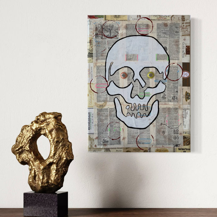 The artwork 'In Vino Veritas' by Jean-Remi Barbier features a bold skull illustration outlined in black against a collaged newspaper background. The skull has distinctive circular eyes, one brown and one yellow, creating a whimsical yet edgy aesthetic. Mixed media technique combines vintage newsprint textures with acrylic paint in a contemporary street art style, measuring 24 x 18 inches.