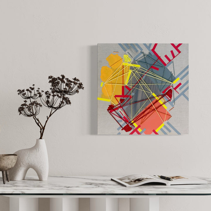 The artwork 'Kaamuura Av.' by Philippe Halaburda features geometric abstract composition with intersecting diagonal lines in yellow, red, and blue-gray tones. Mixed media piece combines bold angular shapes with dynamic yarn elements creating depth and movement. Acrylic paint, tape, and yarn on canvas create textural contrast and contemporary urban aesthetic.