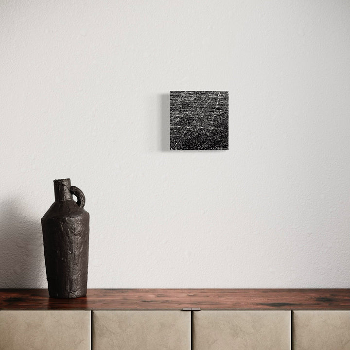 The artwork 'Los Angeles' by Neil Shapiro features a minimalist composition with a black and white aerial map print on textured Hahnemühle paper, displayed above a dark ceramic vessel on a wooden surface. The square print showcases intricate street patterns and urban layout in high contrast monochromatic tones.