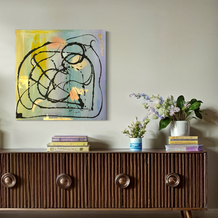 The artwork 'Let It Flow I' by Hazal Ozturk features dynamic black brushstrokes flowing in curved, interwoven lines against a dreamy watercolor background of yellow, mint green, and peach hues. The abstract composition on canvas creates a sense of movement and spontaneity through bold gestural marks and delicate color transitions.