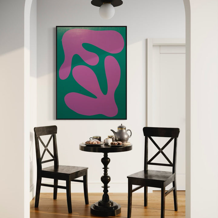 The artwork 'MONSTERA I' by Shadia Sabagh features bold organic shapes in vibrant magenta against a deep emerald green background. Abstract interpretation of monstera leaf forms creates a modern minimalist composition on wood panel, framed in black, shown in a dining nook setting. Acrylic painting measuring 36x48 inches.