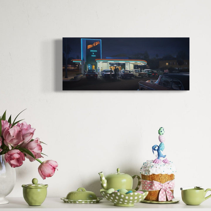 The artwork 'MR. EDS DINER' by Alex Devereux captures a nostalgic nighttime scene of a vintage American diner. The illuminated neon sign glows against a deep blue evening sky, while parked cars silhouette the foreground. The acrylic painting on canvas showcases warm lights from the diner's windows reflecting off the classic car-filled parking lot, creating an atmospheric mid-century Americana aesthetic.