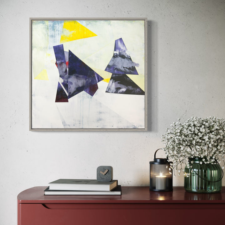 The artwork 'NP X' by Ken Schiano features abstract geometric shapes including a vibrant yellow triangle and deep navy blue angular forms against a stark white background. The composition employs dry pigment and cold wax on canvas, creating textural contrasts and a minimalist aesthetic. The work's modern, angular design showcases sharp edges and geometric interplay. By Ken Schiano.