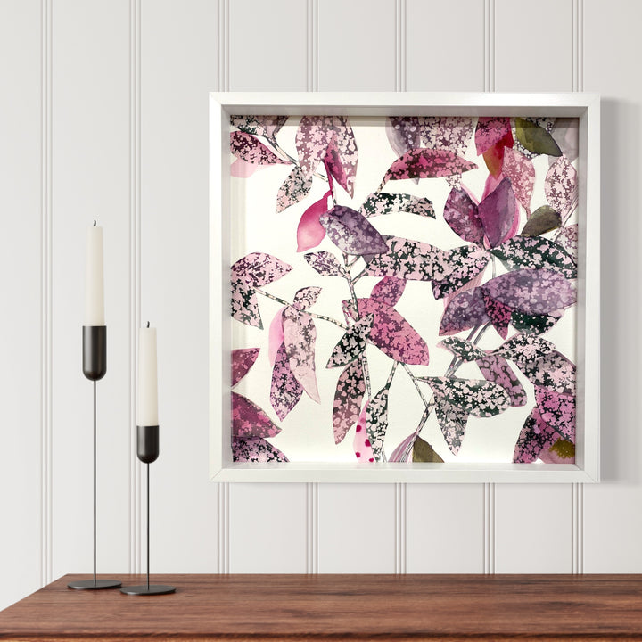 The artwork 'Patterned Garden' by Rachel Kohn features delicate watercolor and ink leaves in shades of purple, pink, and gray scattered across white paper. The abstract botanical composition shows speckled and textured foliage creating a dynamic, floating pattern within a white frame, measuring 21x21 inches. Art by Rachel Kohn.