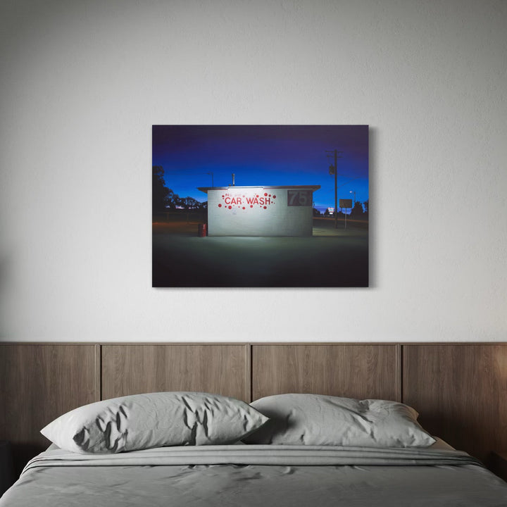 The artwork 'RED DOT' by Alex Devereux captures a nighttime urban scene featuring a white building with red text illuminated against a deep blue sky. The minimalist composition showcases a car wash structure in stark lighting, creating dramatic contrast between light and shadow. The 30x40 inch acrylic on canvas painting emphasizes architectural simplicity and urban solitude.