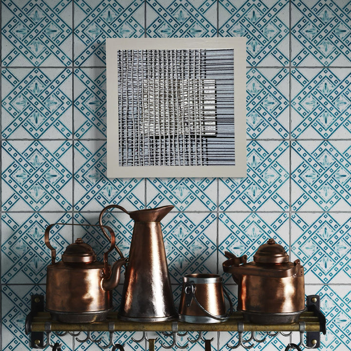 The artwork 'Sentence Structure String 2' by Anne Sherwood Pundyk features a geometric black and white grid pattern printed on bright white paper mounted on wood panel, displayed against a blue and white geometric wallpaper backdrop, with vintage copper kitchenware arranged on a shelf below. The print creates a striking minimalist contrast with its decorative background.