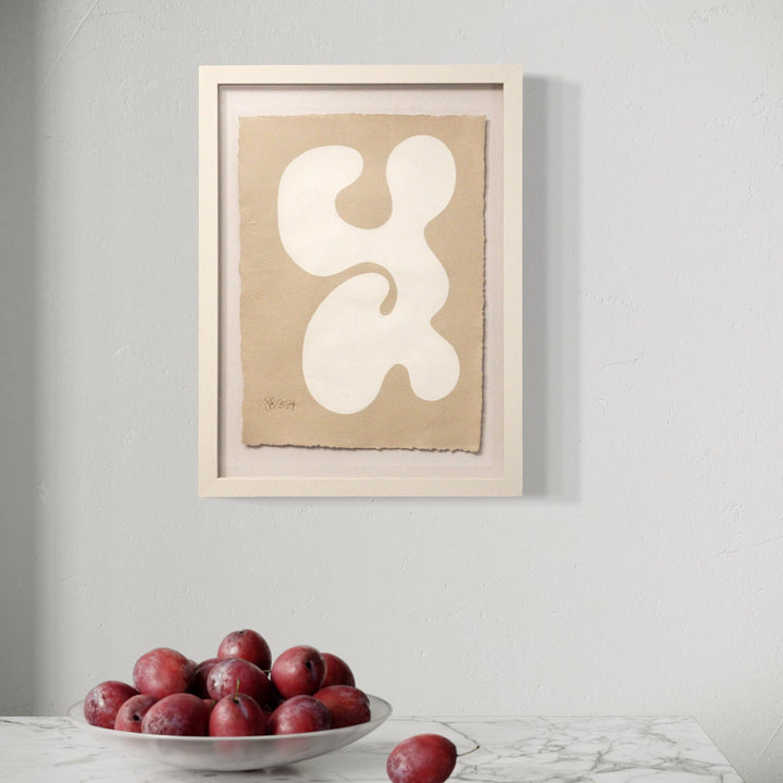 The artwork 'Serenity III' by Shadia Sabagh features an organic abstract shape in pristine white against a warm beige background, painted in acrylic on handmade cotton paper. The flowing, curved form resembles a modernist fluid design, framed in crisp white, creating a minimalist and contemplative composition by Shadia Sabagh.