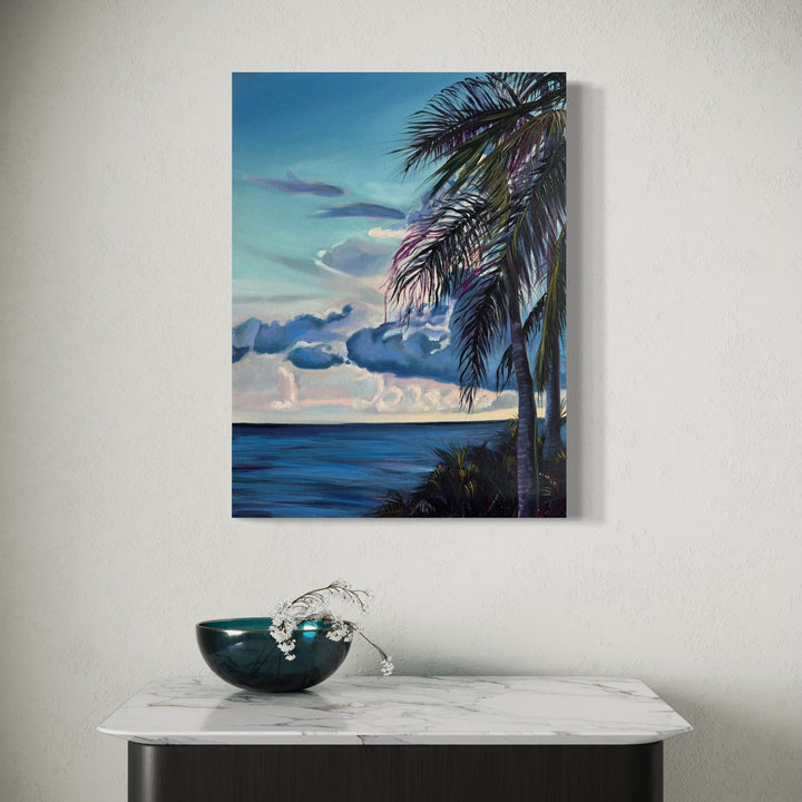 The artwork 'Solitude' by Claudia Robles-Gil features a serene coastal landscape with graceful palm fronds in the foreground against a vibrant turquoise sky. Dark blue ocean waters stretch to the horizon where billowing clouds cast dramatic shadows. The oil and acrylic painting captures a peaceful tropical sunset scene with rich colors and detailed brushwork on an 18x24 inch canvas.