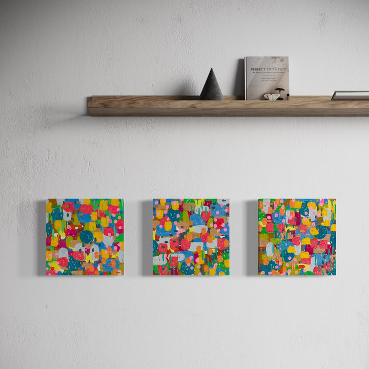 Spring Rooftop Garden Triptych by Alexandra Jamieson features three vibrant 10x10 abstract canvases displaying a kaleidoscope of bright circles and geometric shapes. The composition bursts with playful colors including yellow, blue, pink, and orange, created using acrylic paint and ink with textural gesso elements, arranged in a modern patchwork pattern.