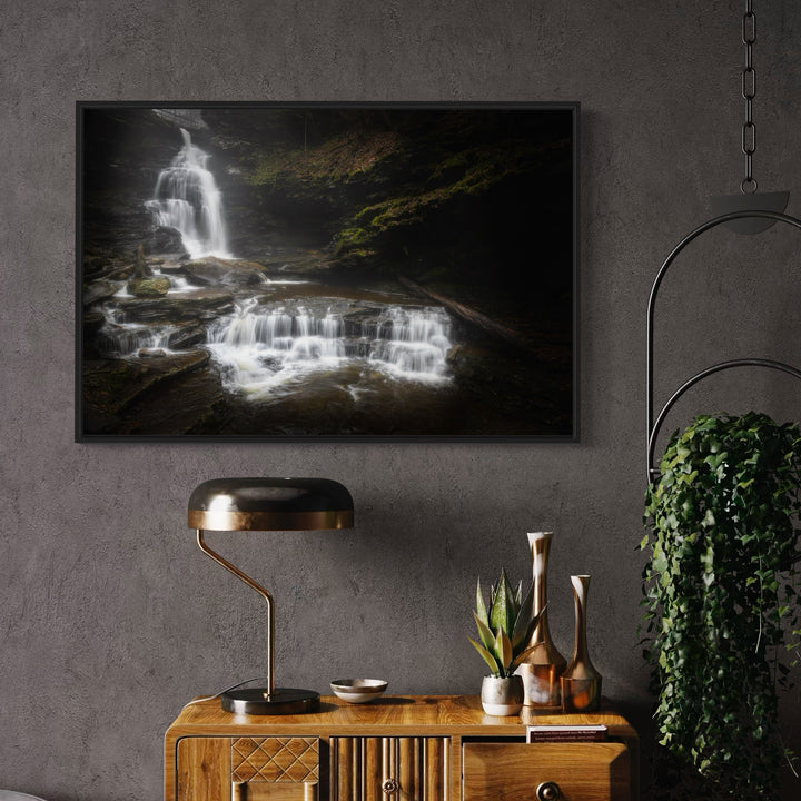 The artwork 'Steps of Eternity' by Dennis Maida captures a dramatic waterfall cascading over dark rocky terrain in multiple tiers, creating a ethereal white mist effect against a moody, shadowed background. The photograph features rich contrasts between the luminous flowing water and moss-covered rocks, showcasing nature's raw beauty in a 24x36 inch fine art print.