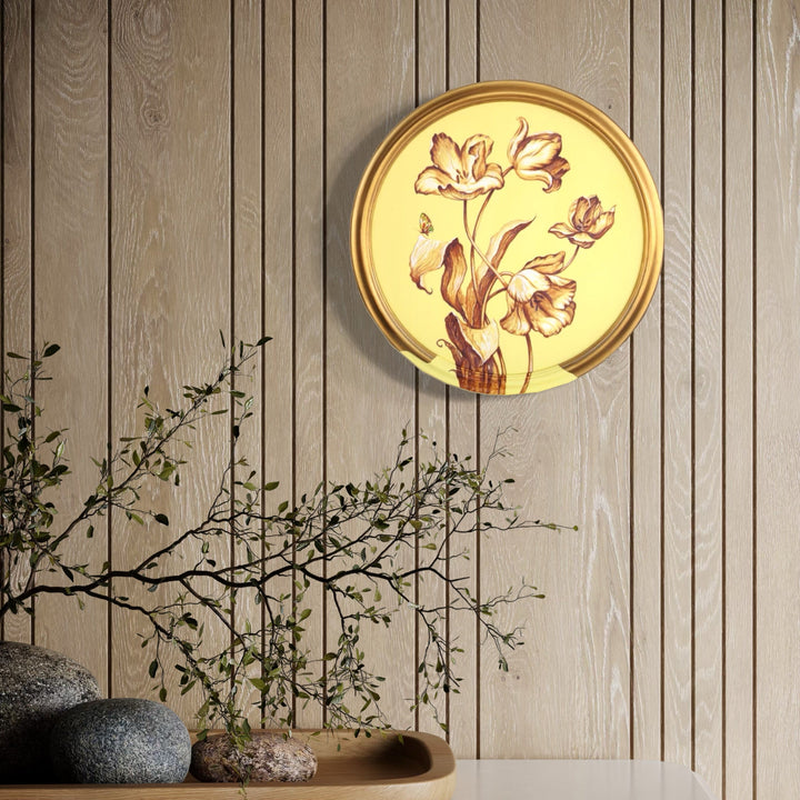 The artwork 'Sunlight' by Carlos Gamez de Francisco features a circular illuminated wall light with delicate floral motifs. Soft pink and brown botanical illustrations of blooming flowers and stems are set against a warm yellow backlight, mounted on a textured beige wood-paneled wall, creating an elegant oriental-inspired ambiance. 16x16 inches acrylic on canvas.