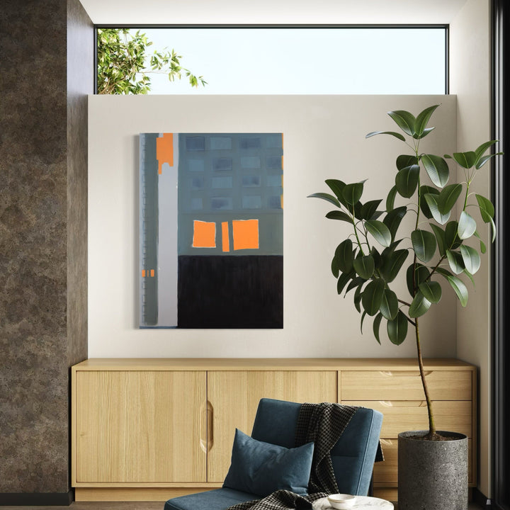 The artwork 'Sunrise in the West 19' by Cora Jane Glasser features a minimalist abstract composition with geometric blocks in steel blue and vibrant orange. The painting displays a bold vertical structure with a dark base, creating a striking contrast against the clean edges and textural oil technique on Arches paper. A contemporary piece that captures urban geometry and morning light.