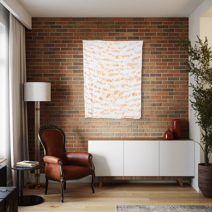 The artwork 'Distorsione di tetto' by Jacqueline Ferrante features abstract wavy patterns in soft peach and cream tones created with coffee and natural pigments on linen. The piece displays organic, rippling lines reminiscent of roof distortions, mounted against exposed brick wall in modern interior setting. Artwork size 48x35 inches by Jacqueline Ferrante.