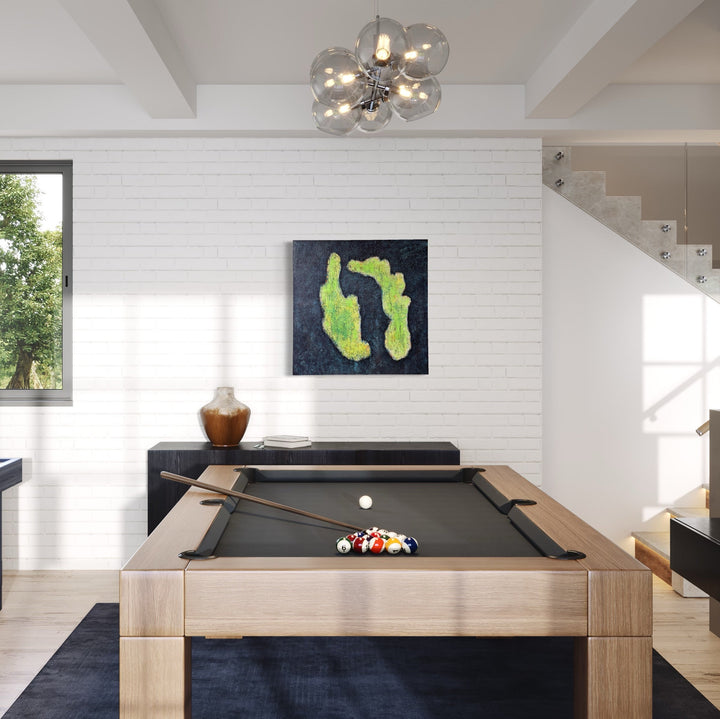 The artwork 'número 54' by Roberto A Godinez features abstract organic shapes in vibrant lime green against a deep navy blue background, displayed above a pool table in a modern interior setting. The oil on canvas piece measures 36x36 inches, creating a striking contrast against white brick walls.