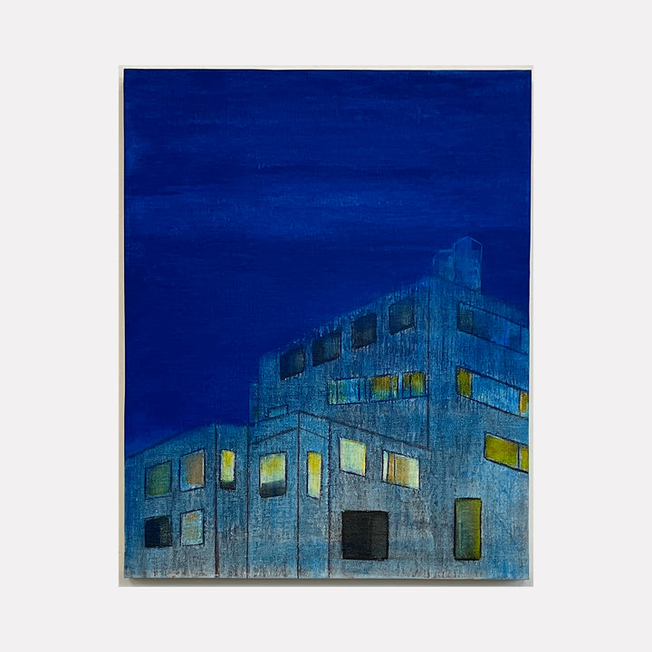 The artwork 'The Blue Hour (enveloping)' by Cora Jane Glasser depicts an abstract urban building at dusk with illuminated geometric windows. The composition features deep indigo blues and warm yellow lighting, rendered in oil on linen. The architectural structure appears textured and modernist against a saturated blue night sky, creating a moody metropolitan atmosphere.