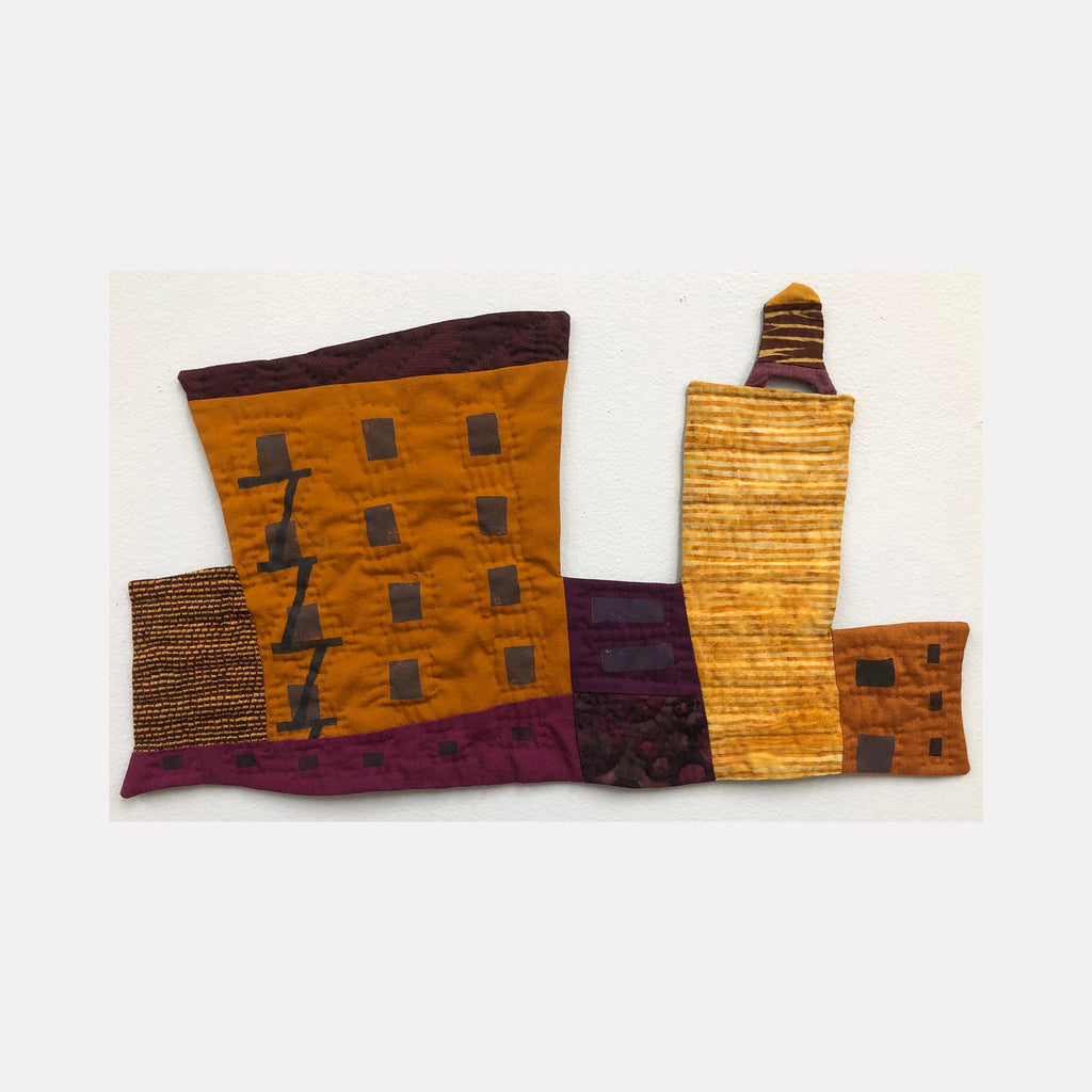 The artwork 'Cityscape (Shades of Gold & Violet)' by Ann Cofta features an abstract urban landscape rendered in quilted fabric. Angular buildings in rich golden ochre and deep violet hues create a stylized skyline. Textural hand quilting and painted details enhance the architectural forms, with small windows dotting the geometric structures against a cream background.