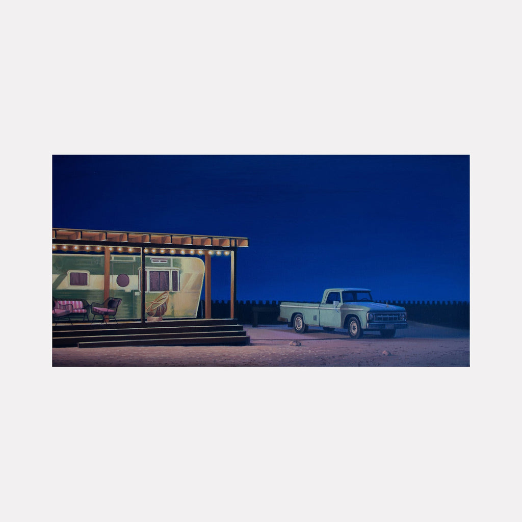 The artwork 'American Dream' by Alex Devereux depicts a nostalgic nighttime scene featuring a vintage mint-green trailer home with a wooden porch and a classic light blue pickup truck. The composition is set against a deep cobalt blue sky, with warm porch lights illuminating the retro dwelling. Acrylic on canvas, measuring 12x24 inches.