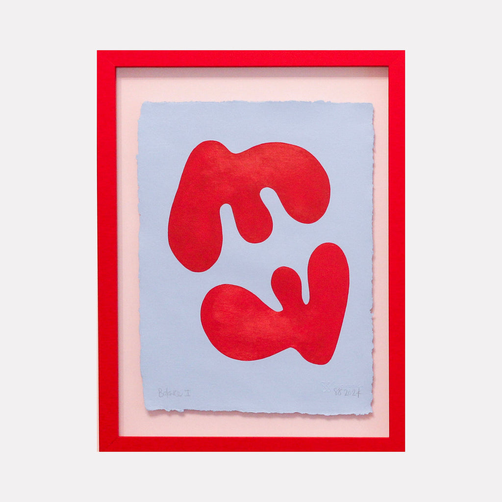 The artwork 'Balance I' by Shadia Sabagh features two bold red organic shapes on a soft blue background, creating a dynamic composition. The abstract forms appear to float and mirror each other, painted in vibrant acrylic on handmade cotton paper with deckled edges, framed in striking red.