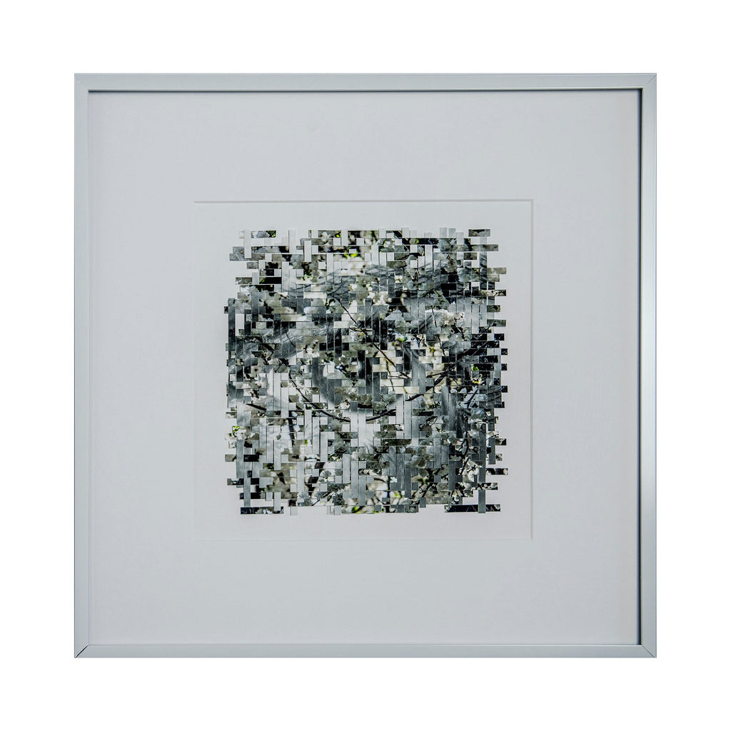 The artwork 'Bloom' by Kiana Honarmand features an intricate mosaic pattern created from hand-cut and woven giclee prints. Abstract black, white, and gray geometric shapes form a complex pixelated composition with subtle yellow accents. The 16x16 inch piece is presented in a minimalist white frame, creating a contemporary digital-meets-traditional aesthetic.