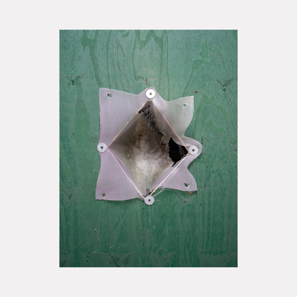 Construction Fence Series-1 by Garrett Carroll: Abstract photographic artwork featuring a geometric opening in a green construction fence, with metallic silver edges forming a star-like shape against a weathered emerald background, capturing industrial minimalism in 24x32 inches photography.