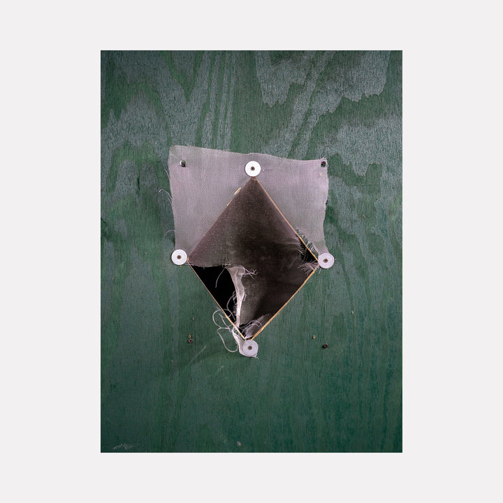 Construction Fence Series-3 by Garrett Carroll: A minimalist photographic study capturing an angular geometric cutout in a green construction fence. The diamond-shaped opening reveals metallic silver tones and industrial fasteners, creating a stark contrast against the weathered green surface.