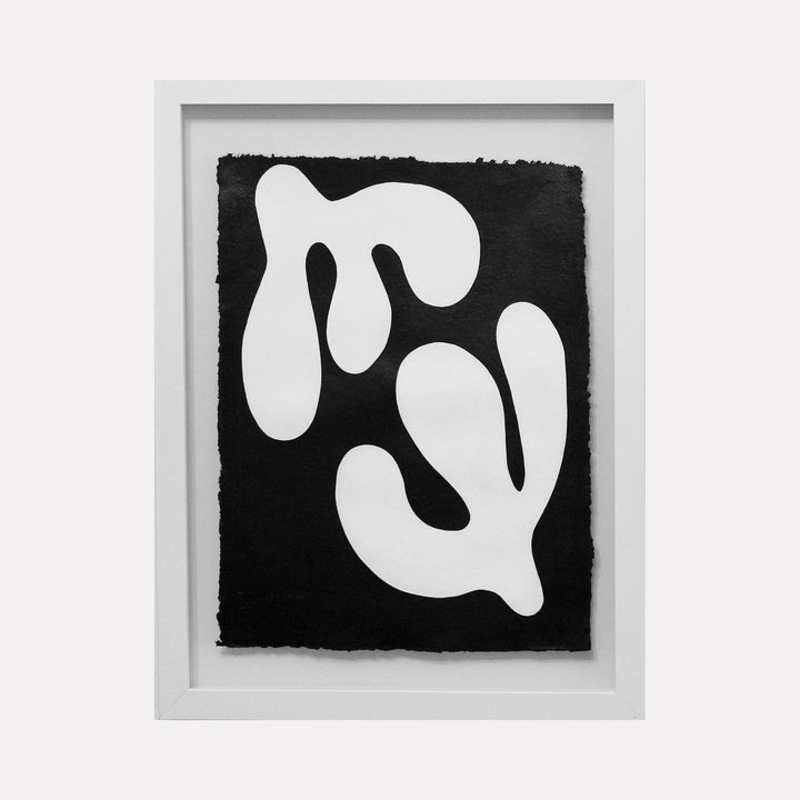 The artwork 'Duality I' by Shadia Sabagh features bold abstract organic shapes in stark white against a deep black background on handmade cotton paper. Two flowing, asymmetrical forms mirror each other, creating a striking contrast and visual balance. The piece showcases minimalist composition with deckle edges, framed in white.