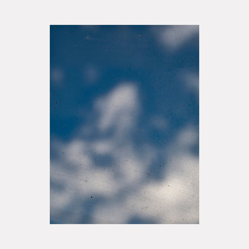 The artwork 'Glimpse Out of a Window - Series-1' by Garrett Carroll captures a dreamy photographic composition of white fluffy clouds against a deep blue sky, viewed through what appears to be a window. The ethereal perspective creates a soft, atmospheric effect with delicate cloud formations floating across the 32x24 inch frame.