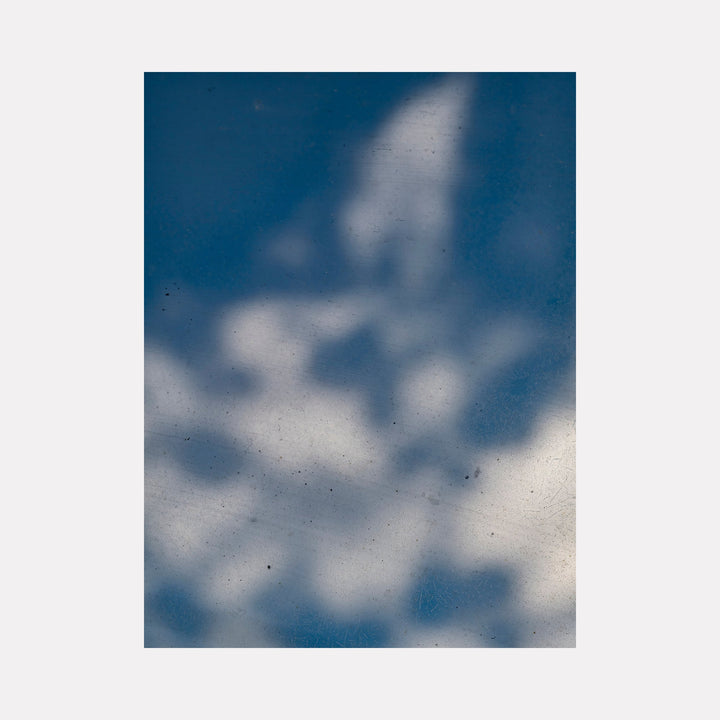 The artwork 'Glimpse Out of a Window - Series-2' captures ethereal shadows and light patterns cast through an unseen window, creating abstract forms against a deep blue background. The photographic composition features soft, cloud-like white shapes with delicate texture and subtle grain. By Garrett Carroll