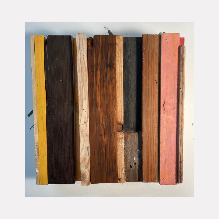 The artwork 'Jabberwock' by Simon Draper features vertical painted wood planks arranged in a geometric composition. The assemblage displays a harmonious palette of yellow, dark brown, natural wood, black, and salmon pink boards, creating a rustic, linear pattern. Each plank shows distinctive weathered textures and rough surfaces, measuring 12x12 inches.