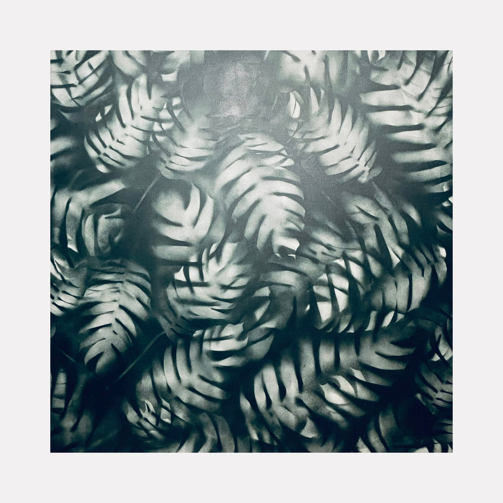 The artwork 'Lush' by Gina Iannucci features overlapping monstera leaf patterns in monochromatic teal and gray tones, created with spray paint on canvas. The leaves create a dynamic, layered composition with a ethereal, misty quality. The 58x58 inch piece showcases a botanical motif with a modern, urban art aesthetic.