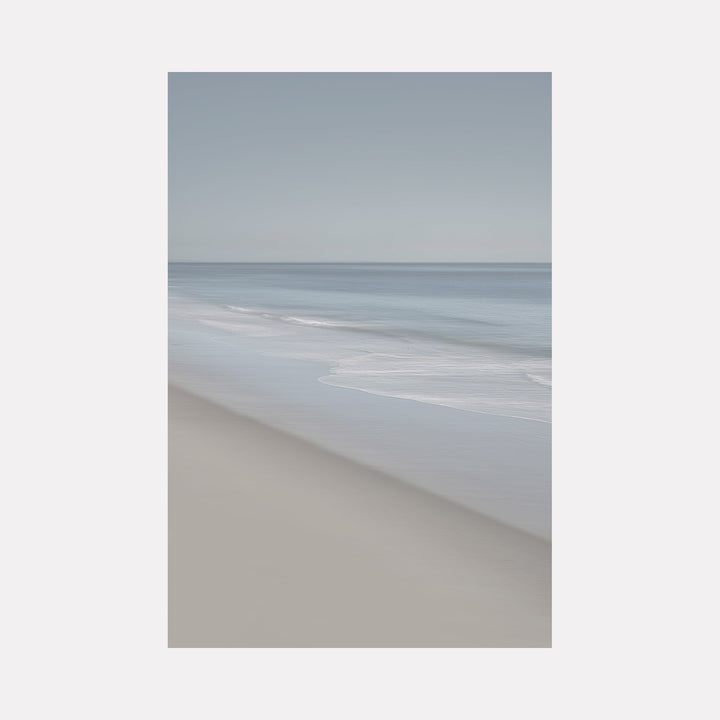 The artwork 'Pacific Shoreline' captures a serene beachscape with gentle waves rolling onto a pristine sandy shore. Subtle blue-grey tones blend with soft beige sand, creating a minimalist coastal atmosphere. The composition features a diagonal shoreline with misty ocean waves, printed on textured Hahnemuhle paper by Neil Shapiro.