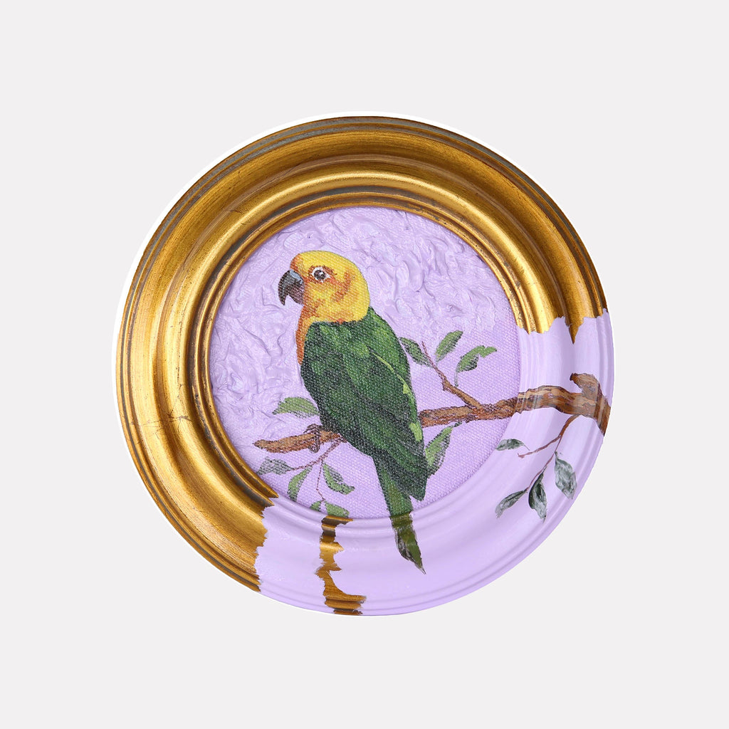 The artwork 'Parrots' by Carlos Gamez de Francisco features a vibrant parrot with yellow head and green body perched on a brown branch against a soft lavender background, enclosed in a circular gold-leaf frame. 5x5 inch acrylic painting on canvas showcases delicate brushwork and ornithological detail.