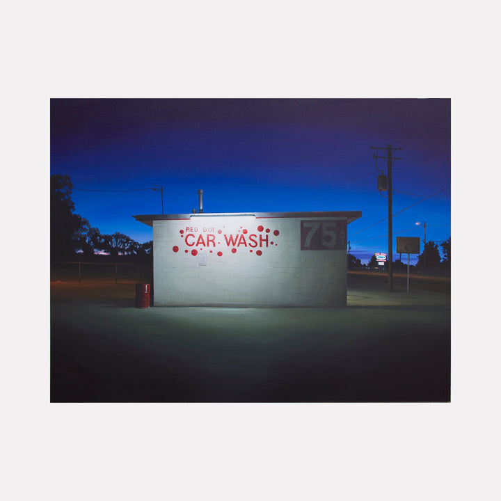 The artwork 'RED DOT' by Alex Devereux captures a minimalist nighttime scene of an illuminated car wash building. The composition features stark white walls against a deep blue twilight sky, with red lettering and dots forming the "CAR WASH" signage. The scene's atmospheric lighting creates dramatic contrast between the building's bright exterior and surrounding darkness, showcasing urban solitude. Acrylic on canvas, 30x40 inches by Alex Devereux