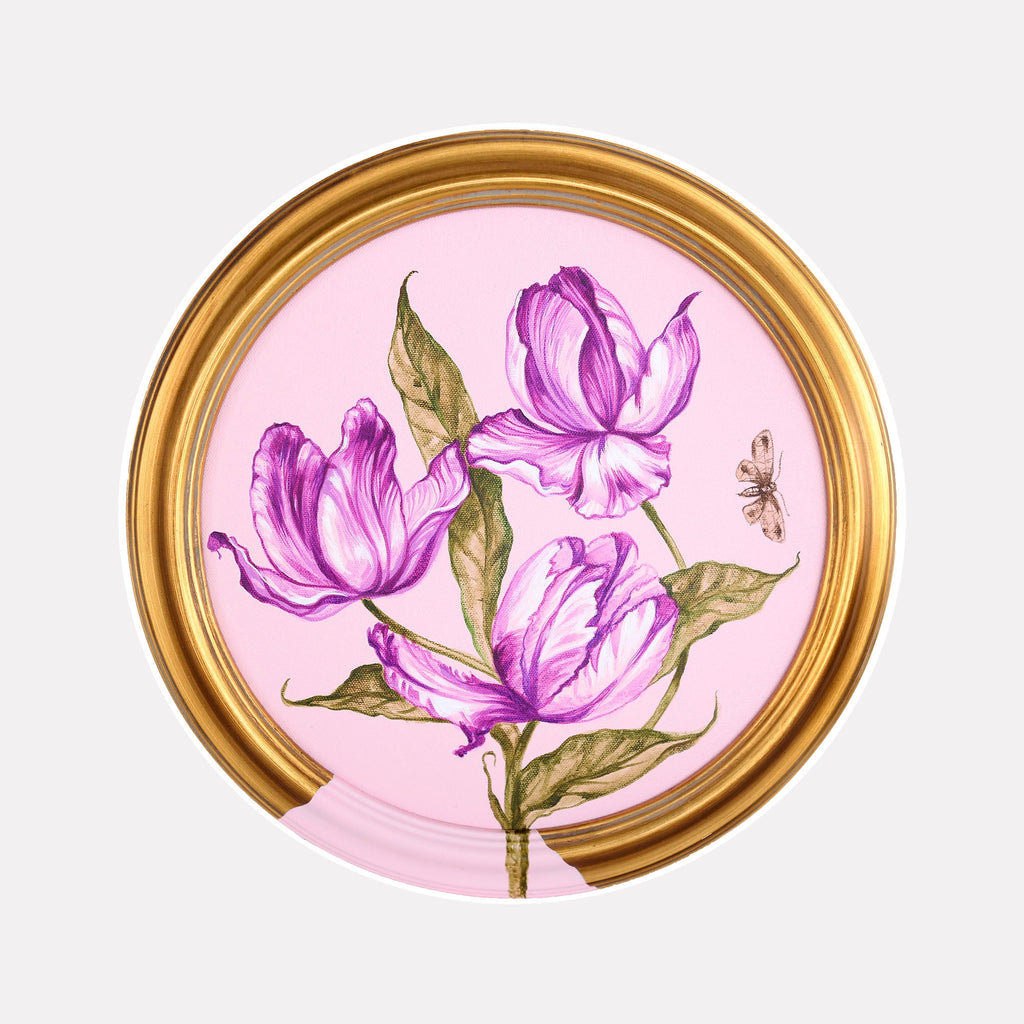 The artwork 'Rose Tulips' by Carlos Gamez de Francisco features three vibrant purple tulips with delicate, layered petals against a soft pink background. The composition is set in a circular gold frame, with olive-green leaves accompanying the blooms. A small bee detail adds natural charm to this acrylic painting, capturing a delicate botanical style on canvas.