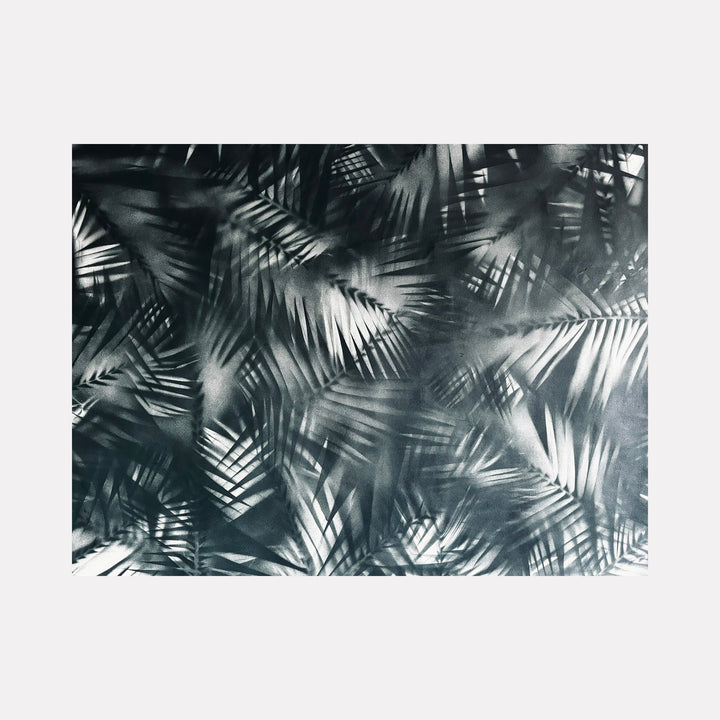 The artwork 'Selva' by Gina Iannucci features overlapping palm fronds in monochromatic spray paint, creating a dramatic interplay of light and shadow. The black and white composition showcases layered tropical leaves in varying opacities, with intricate details capturing the organic patterns of jungle foliage on canvas.