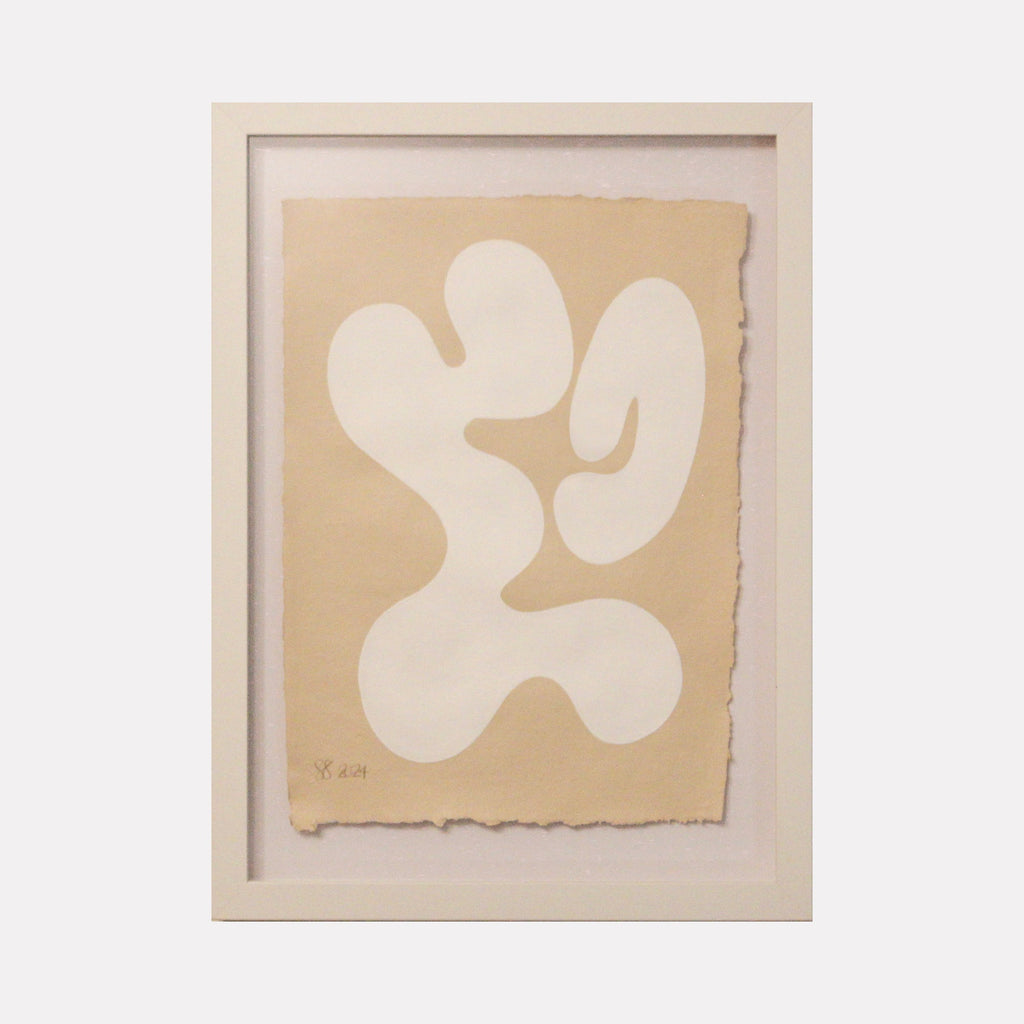 The artwork 'Serenity I' by Shadia Sabagh features an organic abstract form in white against a soft beige background, resembling a flowing, biomorphic shape with curved edges. Created with acrylic on handmade cotton paper, the minimalist composition exhibits a gentle, fluid movement within a white frame.