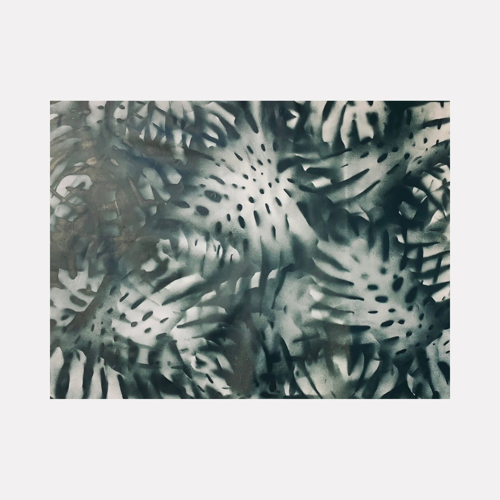 The artwork 'Sombra' by Gina Iannucci features abstract spray-painted patterns in monochromatic gray tones, creating a dynamic tropical leaf motif. Organic shapes reminiscent of monstera leaves overlap and blend, producing a shadowy, ethereal effect on gallery canvas. The 36x48 inch piece combines soft and sharp edges in a contemporary botanical design.